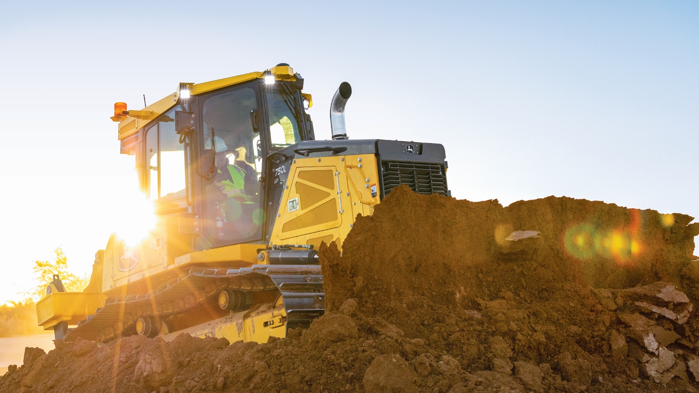 Bouteur 750L SmartGrade poussant de la terre tandis que le soleil se lève derrière la machine.