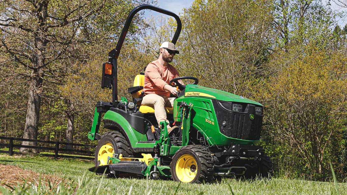 Man riding a 1025r tractor near a fence and some trees