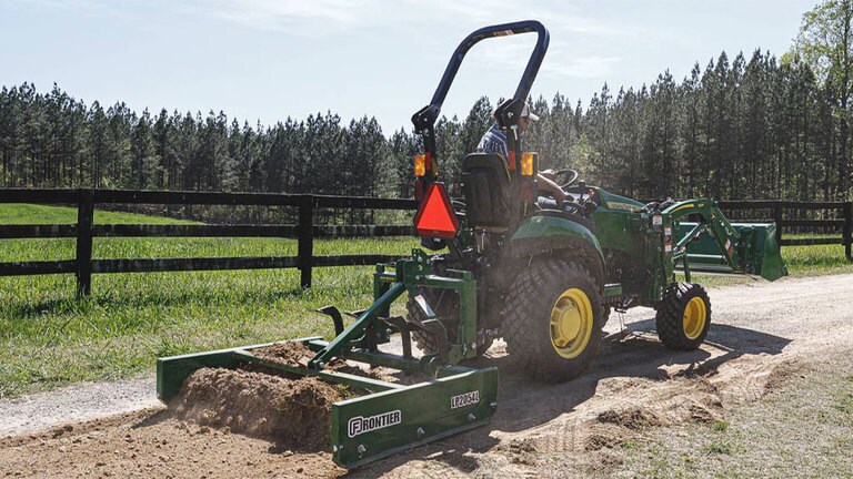 Homme nivelant une route de terre avec un tracteur 1025R