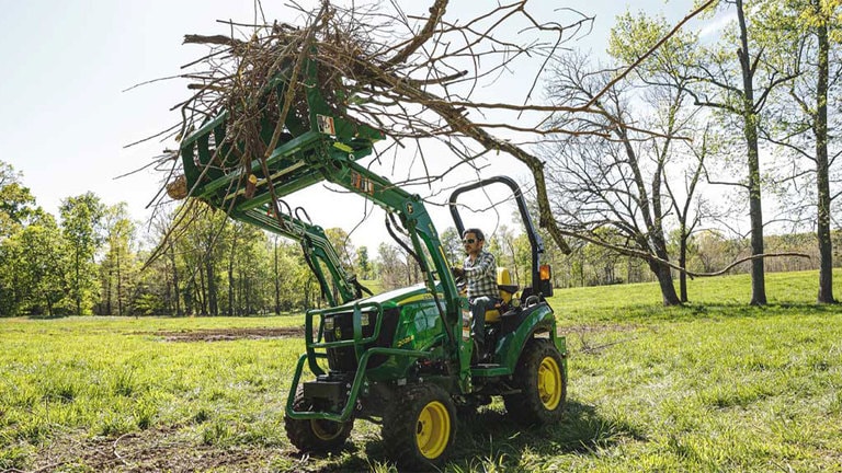 Homme tenant une pile de bâtons en l’air à l’aide d’un tracteur 2025R