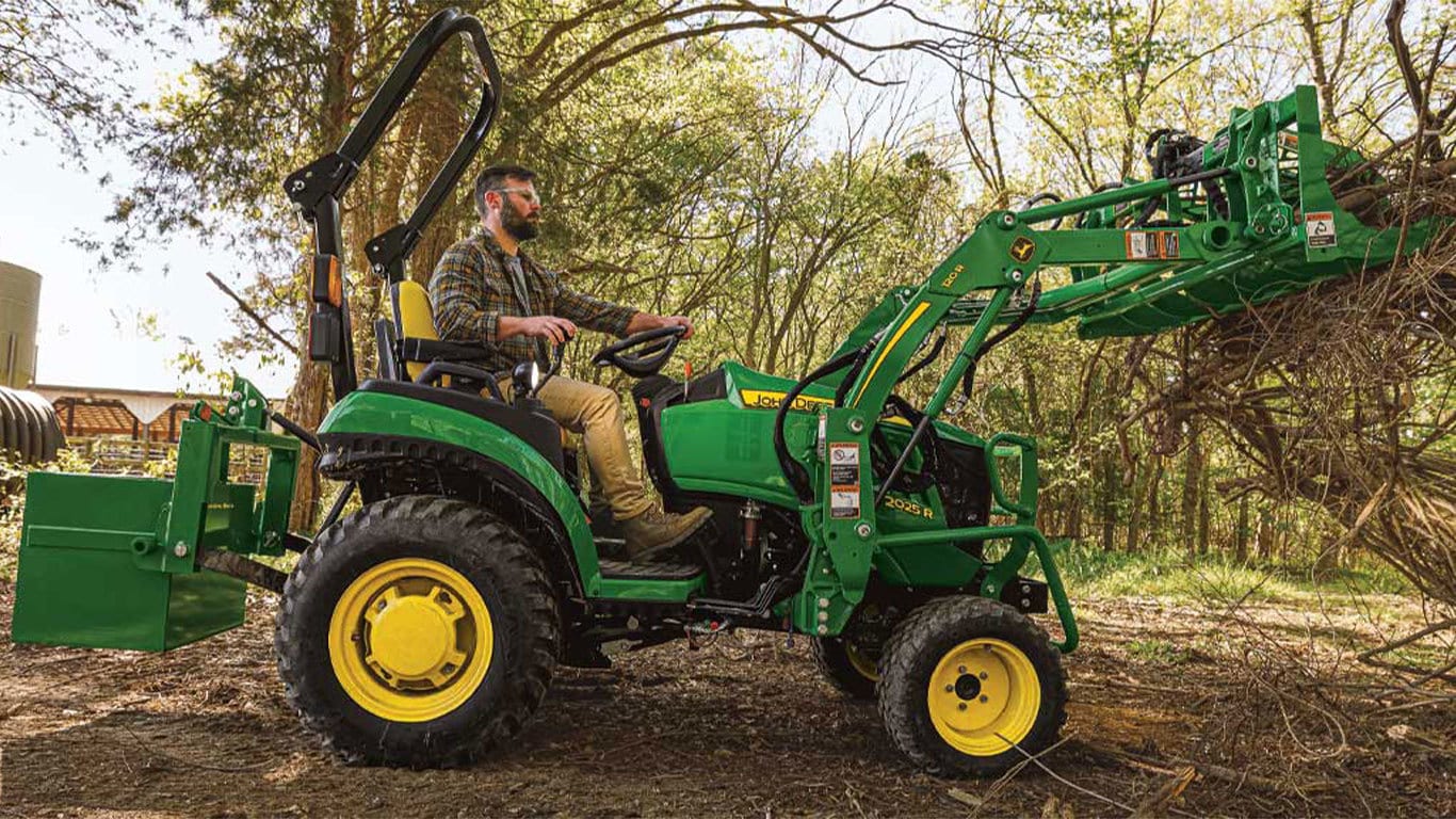 Man moving a pile of sticks with a 2025r tractor