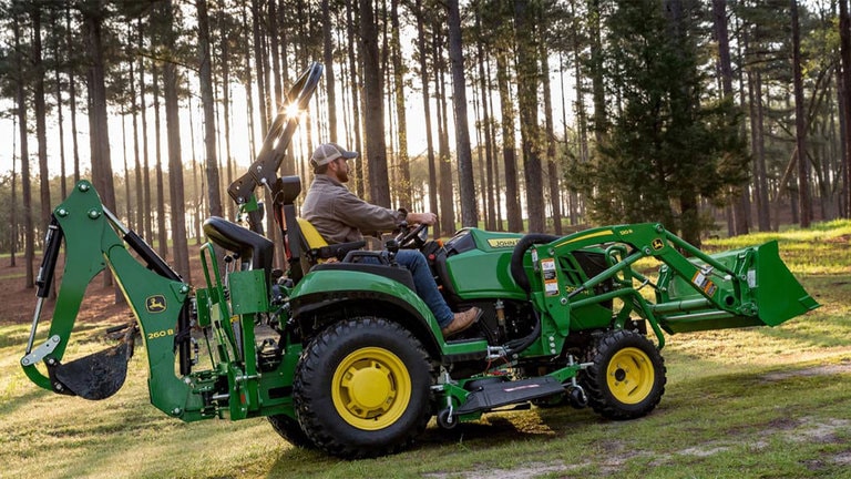 Man driving a 2025r tractor in front of a wooded area