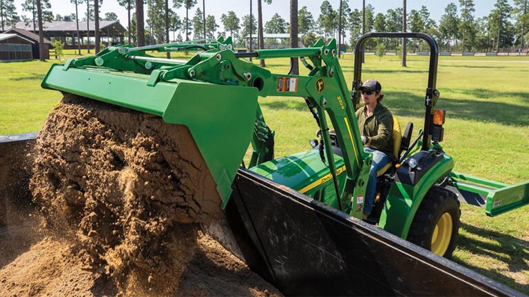 Man dumping dirt into a truck bed with a 2032r tractor