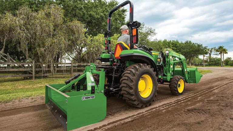 Man grading a dirt road with an attachment on the back of a 2038r tractor