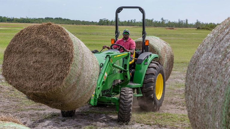 Man driving 4044m tractor picking up a hay bale