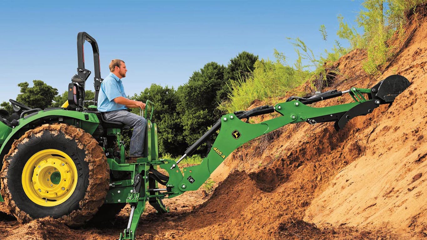 Homme conduisant un 4044R en haut d'une colline avec un équipement ramassant la saleté