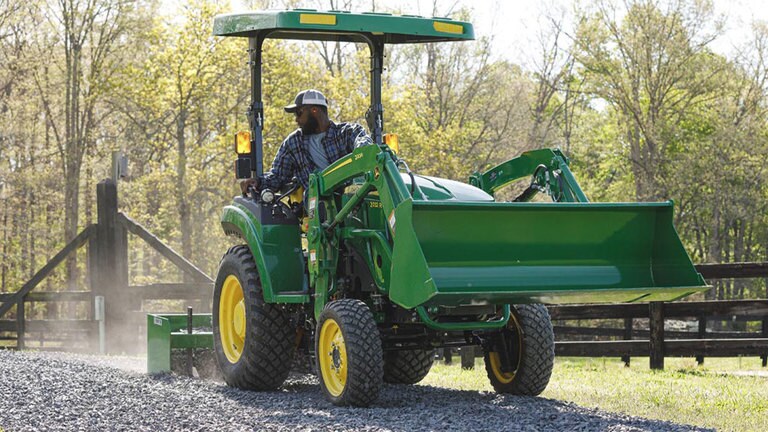 Homme nivelant la route de gravier avec un tracteur 2032R