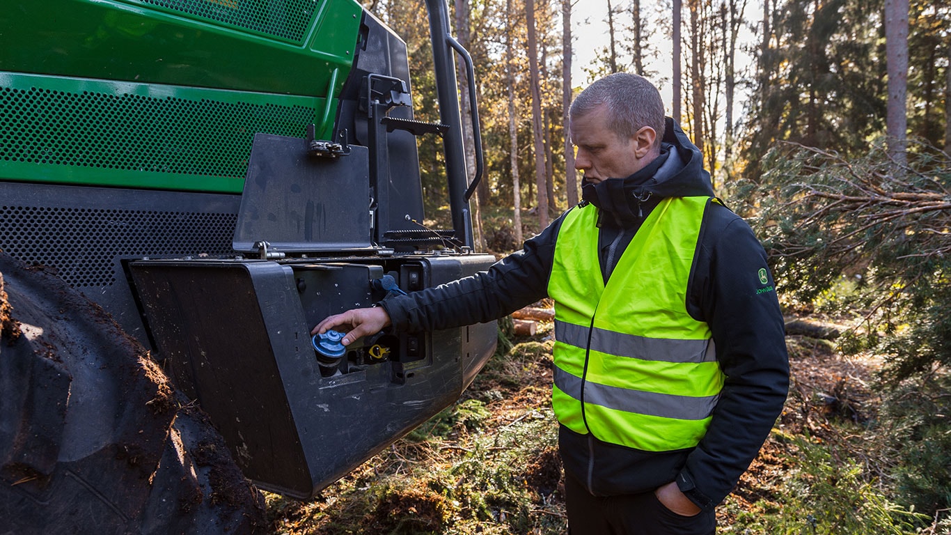 Technicien assurant l’entretien de la machine forestière John Deere de la série H, avec compartiment moteur ouvert.