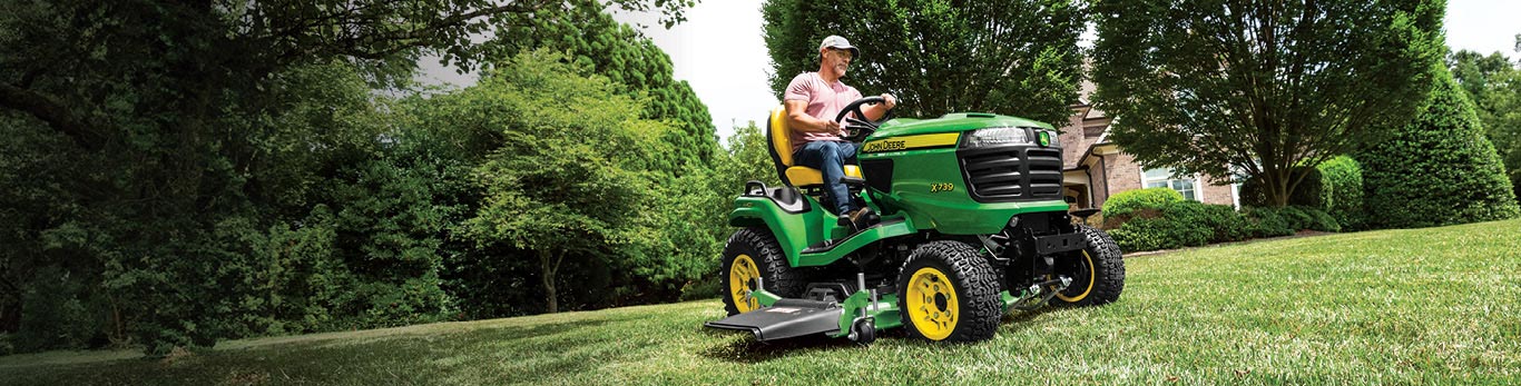 Woman in the seat of a John Deere X739 riding lawn mower cutting grass.
