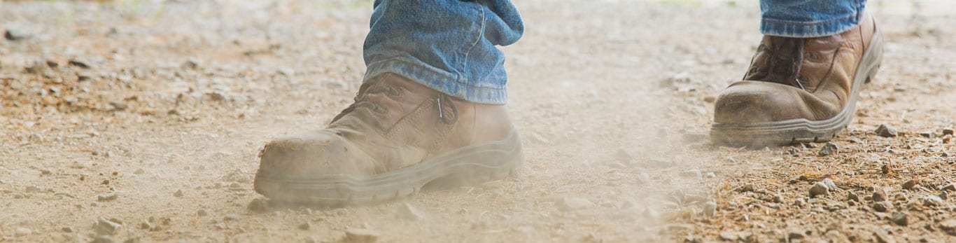 Paire de bottes d’une personne marchant dans un champ en faisant lever la poussière