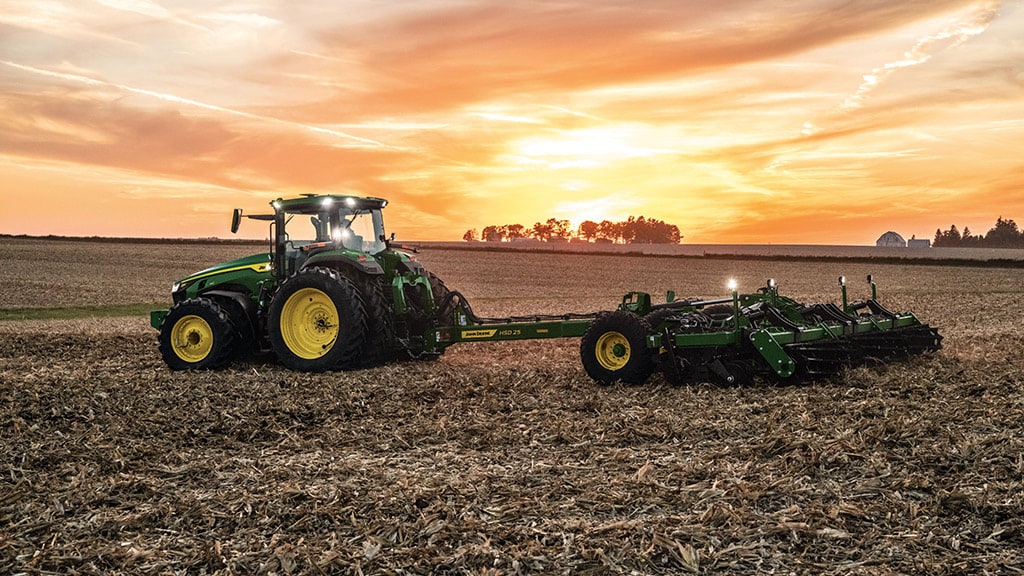 Tracteur 8R tirant un outil de labourage au coucher du soleil.