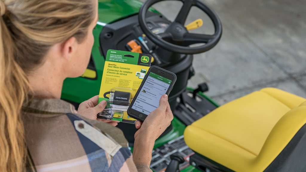 Woman standing beside a lawn mower holding an hour meter connector and her cell phone