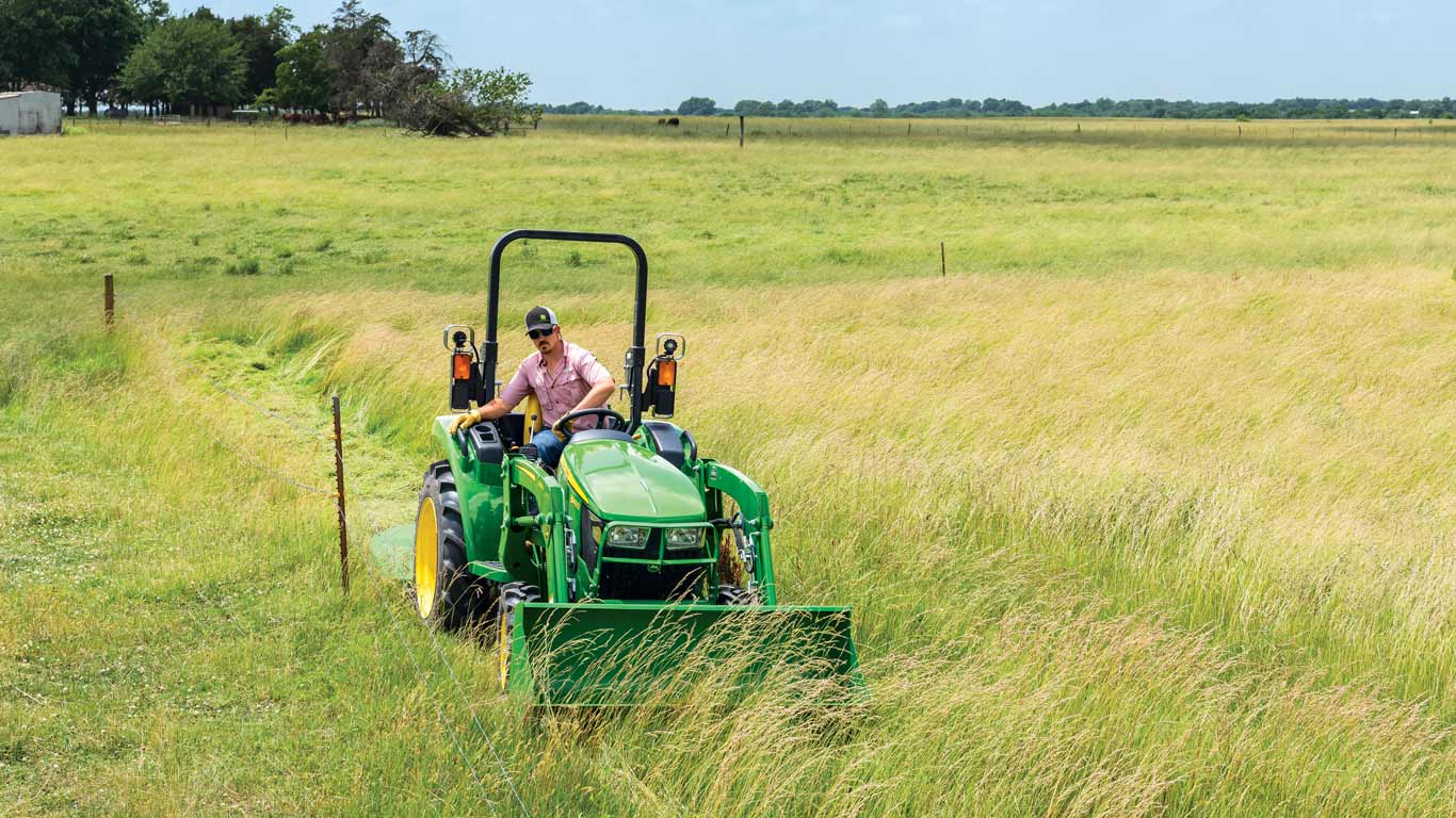 un homme conduisant un tracteur compact John Deere 3043D dans un pâturage
