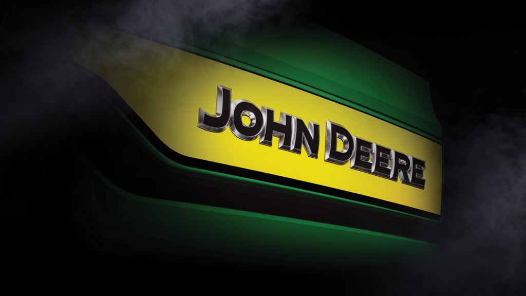 Close-up of a 3D John Deere wordmark with raised black letters and chrome edges on yellow-green panel