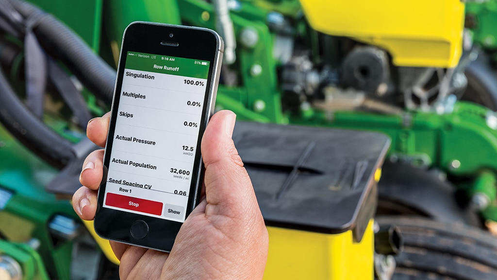 Téléphone intelligent montrant les paramètres de l’application agricole, avec un équipement agricole en arrière-plan.