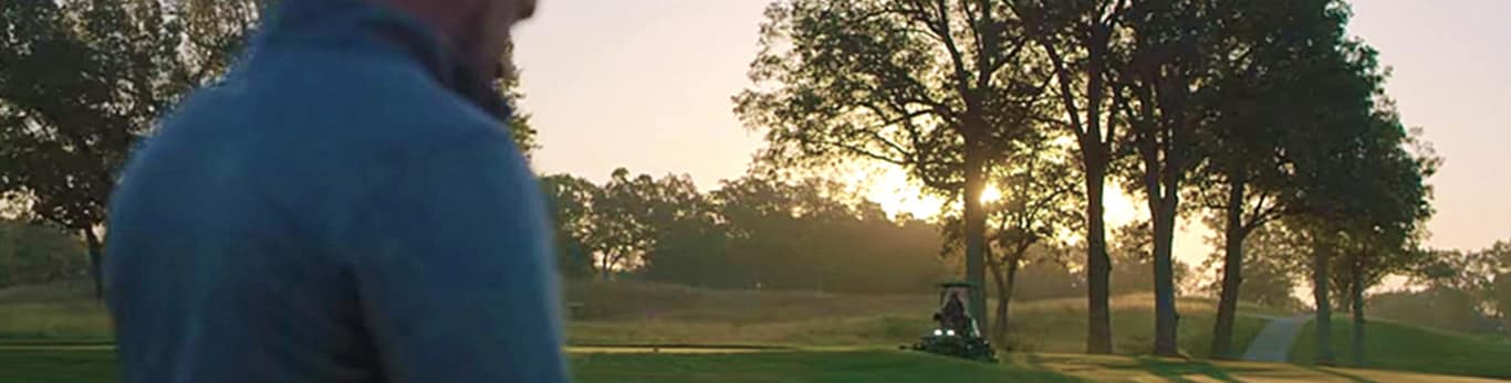 Image of a person with a cellphone on a golf course with a fairway mower in the background