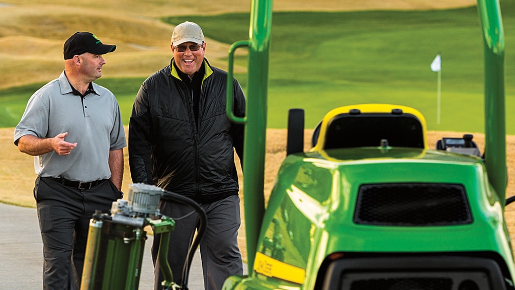 2 men walking towards a fairway mower on a golf course