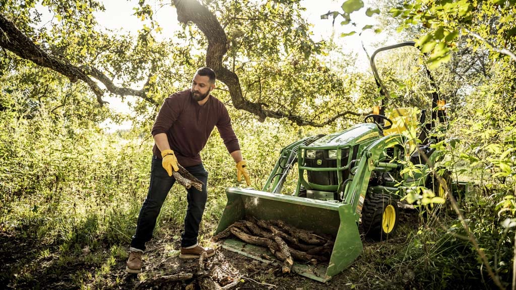 person loading tree branches into front loader attached to lawn tractor in the woods