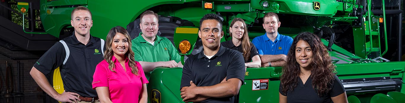 Groupe d'employés se tenant à côté d'une moissonneuse-batteuse John Deere