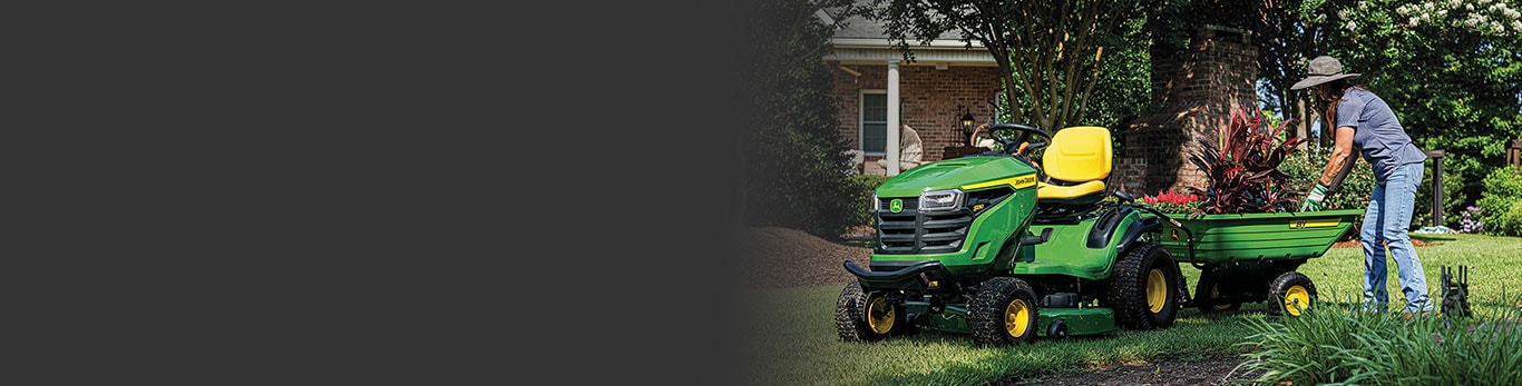 Person in a garden picking up plants from a cart attached to riding lawn mower