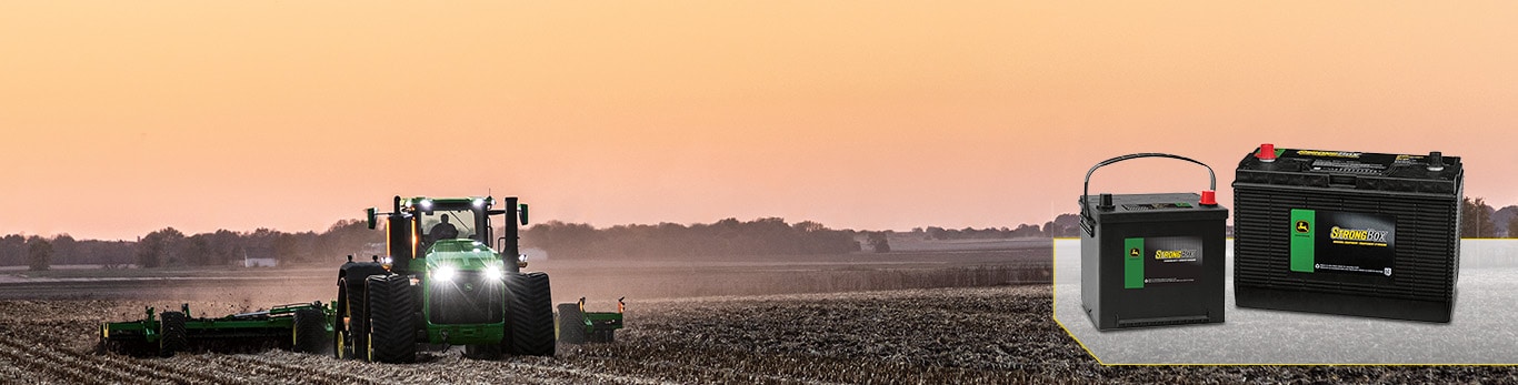 Tractor working in a field at sunset with two John Deere StrongBox batteries shown on the right.