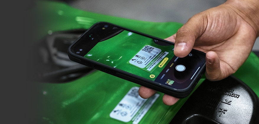 Hand holding a smartphone to scan a QR code on a green equipment label.