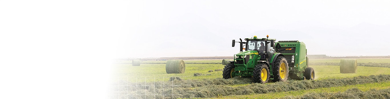 Tracteur John Deere remorquant une rotopresse dans un champ de foin.