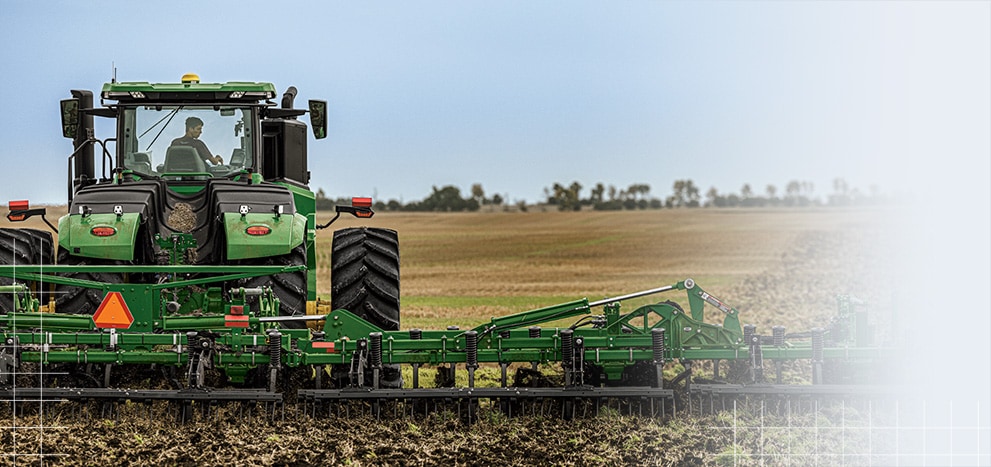 Tractor operating in a field with a tilling attachment.