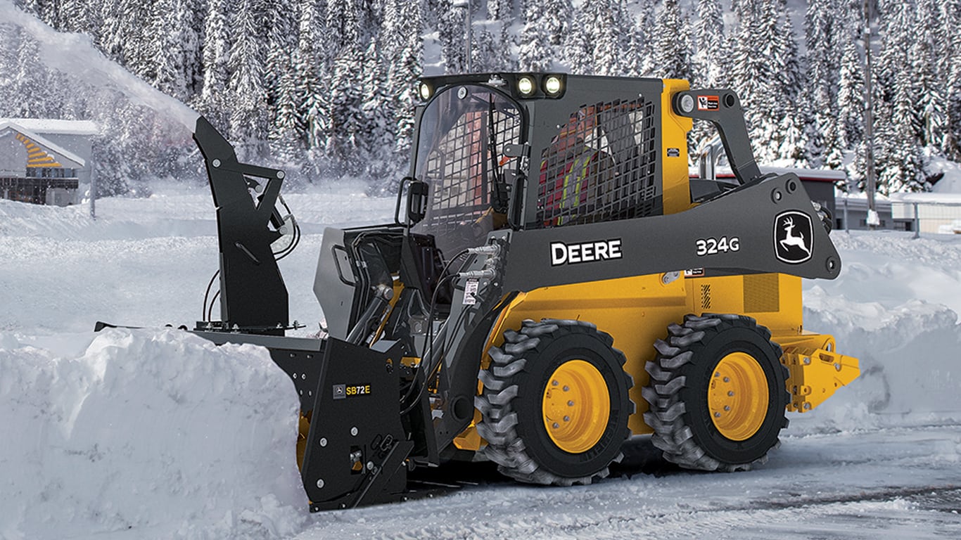 Un volant à patin 324G avec fixation de souffleuse à neige SB72E soufflant de la neige sur une route.