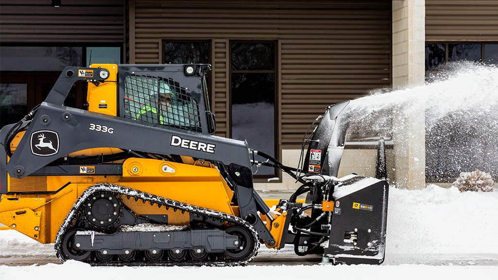 Personne déneigeant avec un tracteur utilitaire équipé d’une souffleuse à neige et d’une chargeuse.