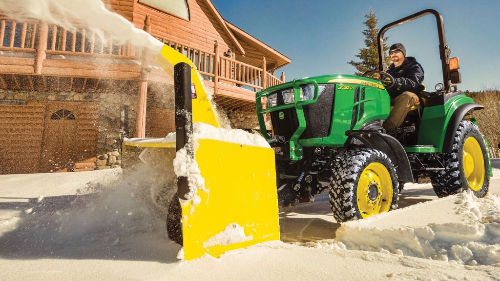 Person clearing snow with a compact utility tractor with snowblower attachment.