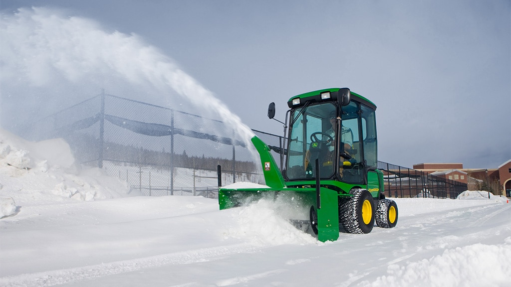 Personne déblayant la neige de l’entrée d’une école à l’aide d’une tondeuse frontale avec souffleuse à neige