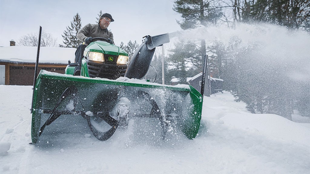 Une personne utilisant un tracteur de pelouse équipé d’une souffleuse à neige pour déblayer une allée.
