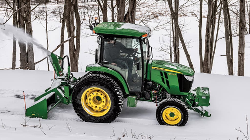 Tracteur compact 4075R muni d'une souffleuse à neige Frontier™ montée à l'arrière soufflant de la neige
