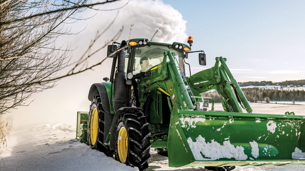 Personne déneigeant avec un tracteur utilitaire équipé d’une souffleuse à neige et d’une chargeuse.