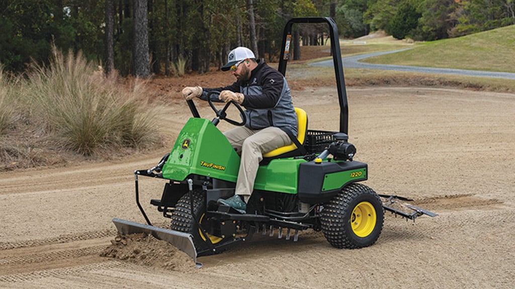 Un homme racle du sable sur un terrain de golf avec un râteau à usage général TruFinish™ 1220