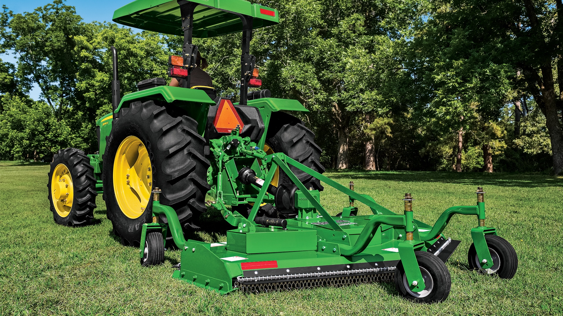 JD grooming mower attached to tractor in field