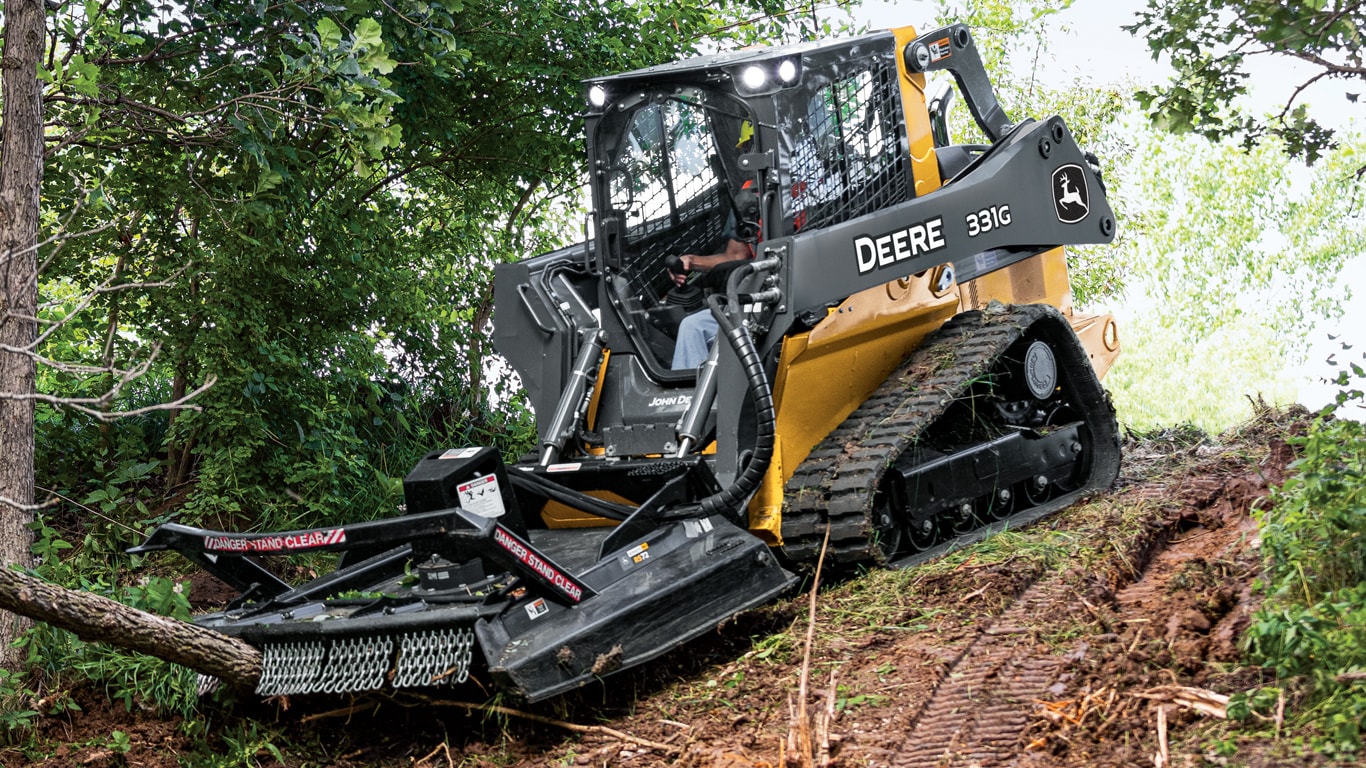 Un chargeur sur chenilles compact 331G défrichant arbres et brosse avec la fixation RS72 Extreme Duty Rotary Cutters.