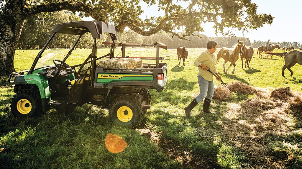 woman shoveling hay into a work series Gator™ in a field