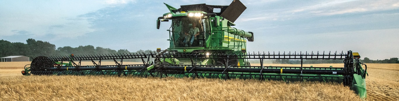 Photo grand-angle de face d’une moissonneuse-batteuse S7 John Deere récoltant du blé avec une tête de coupe de tablier à toile.