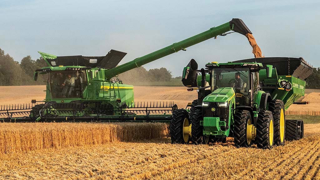 Photo d’une moissonneuse-batteuse S7 John Deere récoltant du blé avec une tête de coupe de tablier à toile, tout en déchargeant des grains dans une remorque à grain tirée par un tracteur John Deere.