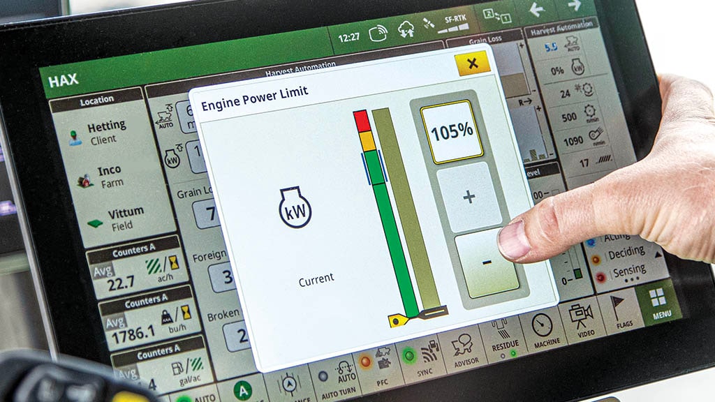 Photo gros plan d’un afficheur G5Plus montrant la main d’un agriculteur modifiant les réglages des limites de puissance moteur, une fonction de la technologie de gestion intelligente de la puissance pour la récolte.