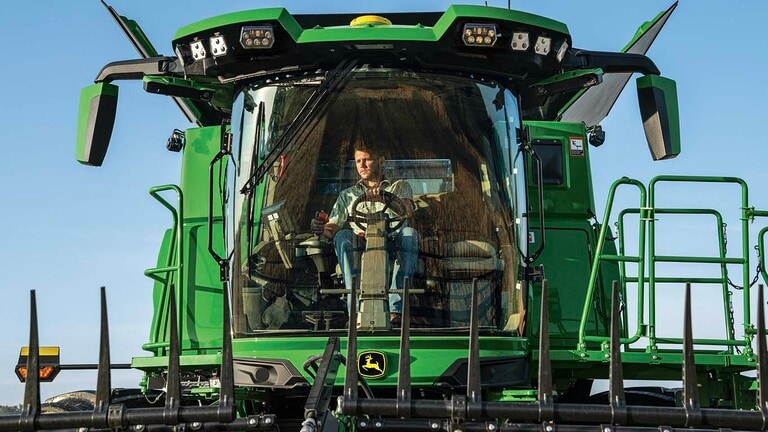 Front view of S7 600 combine cab with farmer steering with one hand and joystick in other