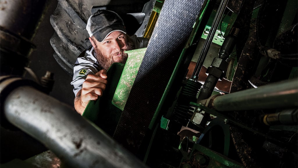 Photo of a John Deere technician performing an inspection on a John Deere Combine