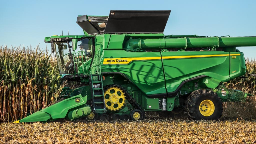 Photo d’une moissonneuse-batteuse X9 John Deere avec chenilles avant récoltant du maïs avec un cueilleur à maïs.