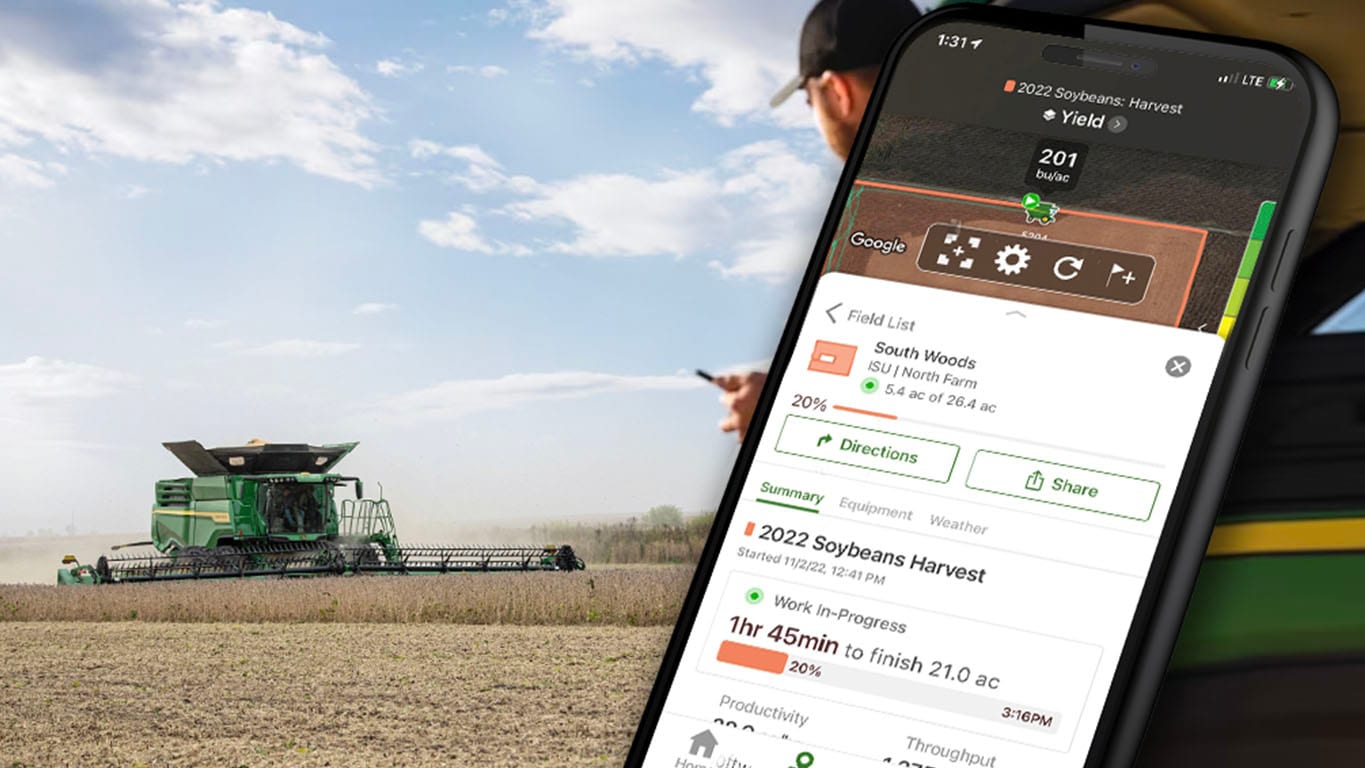 Photo of a farmer leaning against a John Deere Gator, while checking out Operations Center on his mobile device. You can see a John Deere Combine in the background