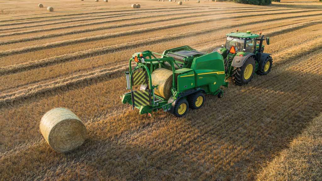 A baler in a field creating 4 foot by 5 foot bales