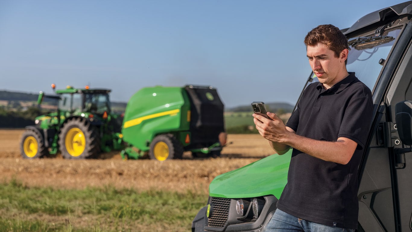 A person viewing their phone with a tractor and baler in the background