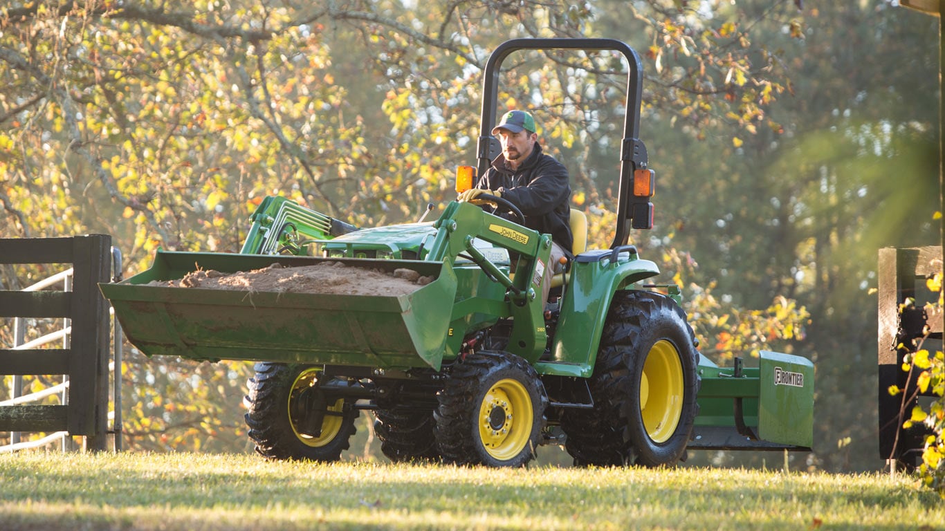 man driving tractor with loader down dirt road