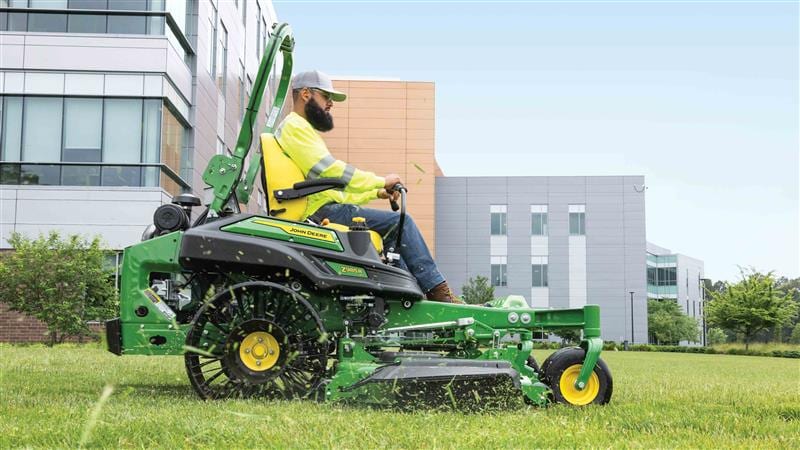 Un travailleur conduisant une tondeuse à zéro rayon dessiné EFI verte avec des pneus sans air sur un campus.